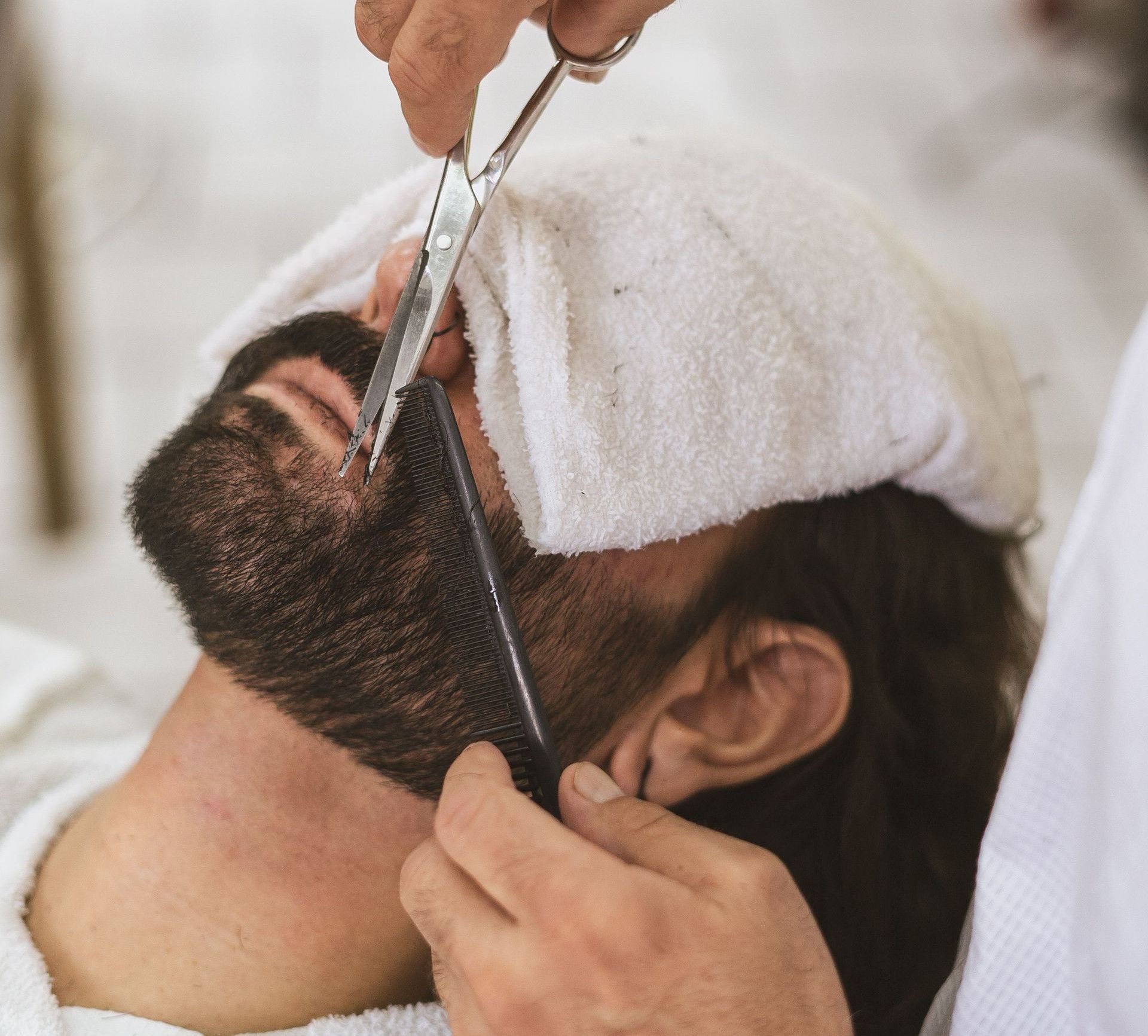 Close-up of a barber trimming a client's beard with scissors and comb.